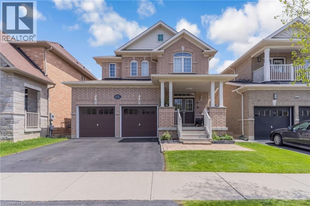 Brick exterior with stone accents, featuring a covered front porch with white columns, a double garage with dark wood-finish doors, an arched window on the second story, and a paved driveway - 675 Best Road, Milton, ON - Outdoor With Facade