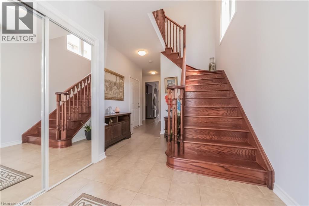 Foyer featuring a hardwood staircase with traditional balusters, neutral tile flooring, and a sliding mirrored closet door - 675 Best Road, Milton, ON - Indoor Photo Showing Other Room
