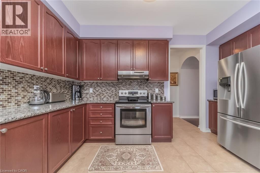 Kitchen featuring extensive wood-finish cabinetry, stainless steel appliances, a mosaic tile backsplash, and light-toned tile flooring - 675 Best Road, Milton, ON - Indoor Photo Showing Kitchen