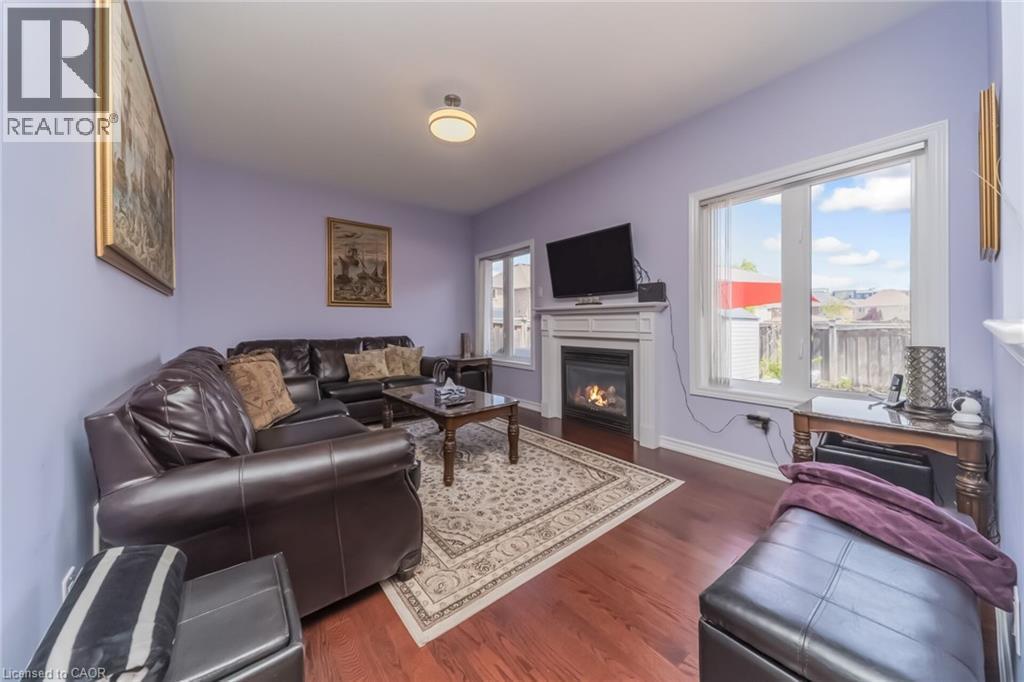 Living area featuring wood-finish flooring, a fireplace with a white mantel, and multiple windows for natural light - 675 Best Road, Milton, ON - Indoor Photo Showing Living Room With Fireplace