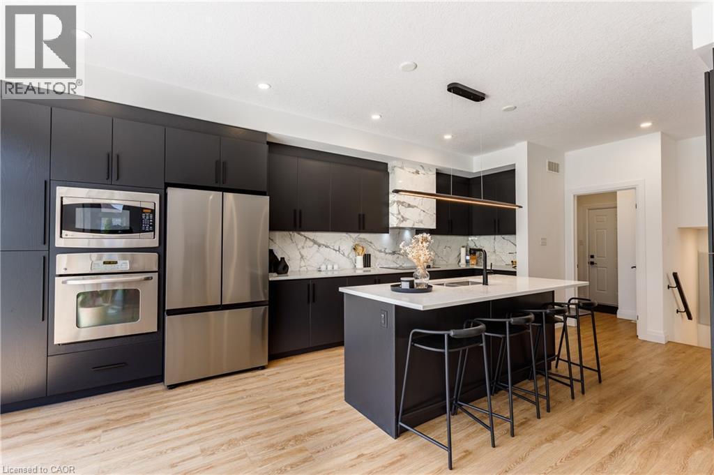 Contemporary kitchen featuring dark flat-panel cabinetry, stainless steel appliances, a center island with seating, and wood-finish flooring - 916 Steepleridge Court, Kitchener, ON - Indoor Photo Showing Kitchen With Stainless Steel Kitchen