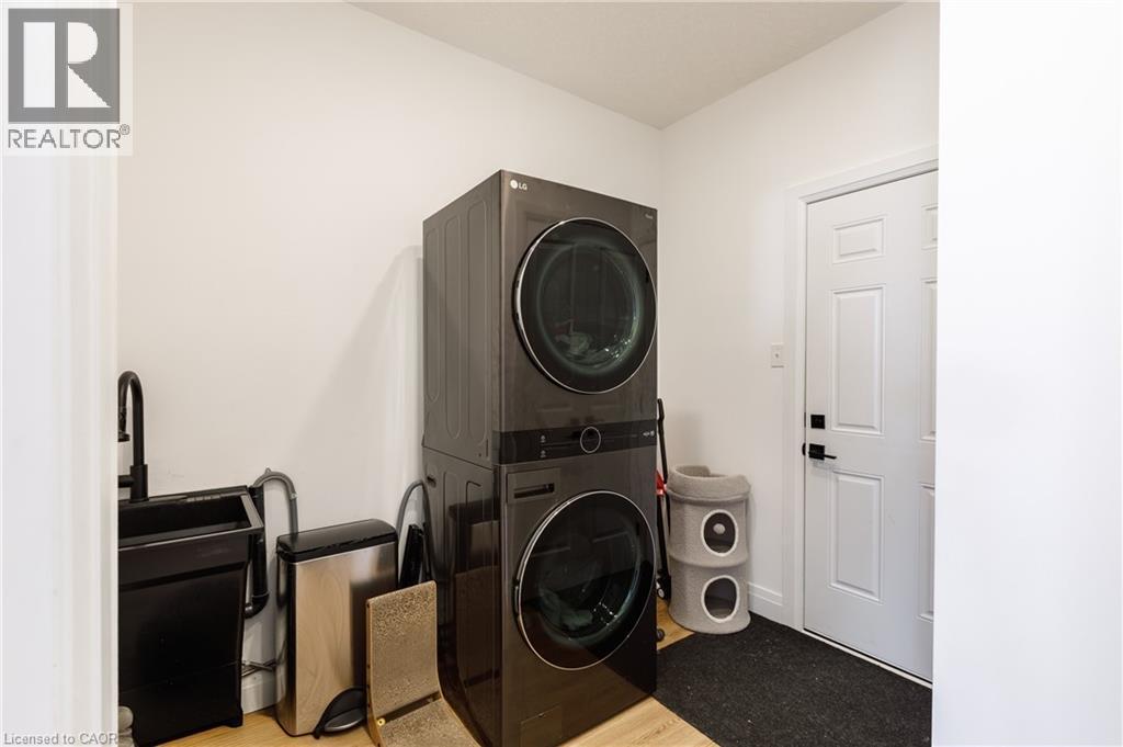 Dedicated laundry area featuring a stacked washer and dryer, a utility sink with a matte black faucet, light wood-finish flooring, and a white panel door with black hardware - 916 Steepleridge Court, Kitchener, ON - Indoor Photo Showing Laundry Room