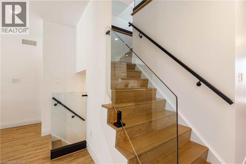 Modern staircase featuring clear glass railings, light wood-finish treads, and a matte black handrail - 916 Steepleridge Court, Kitchener, ON - Indoor Photo Showing Other Room