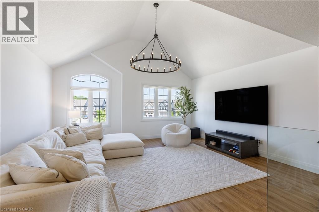 Spacious secondary living area featuring a vaulted ceiling, large arched window, wood-finish flooring, and a contemporary chandelier - 916 Steepleridge Court, Kitchener, ON - Indoor Photo Showing Living Room