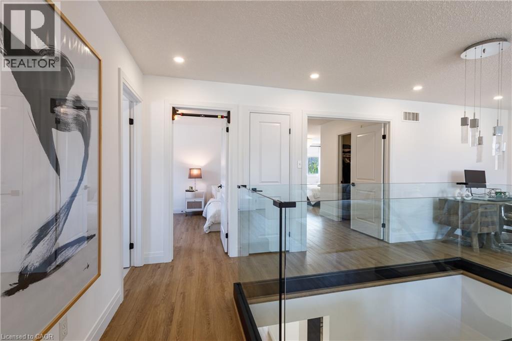Upper-level landing featuring wood-finish flooring, recessed lighting, white walls, a glass railing, and a contemporary multi-pendant light fixture - 916 Steepleridge Court, Kitchener, ON - Indoor