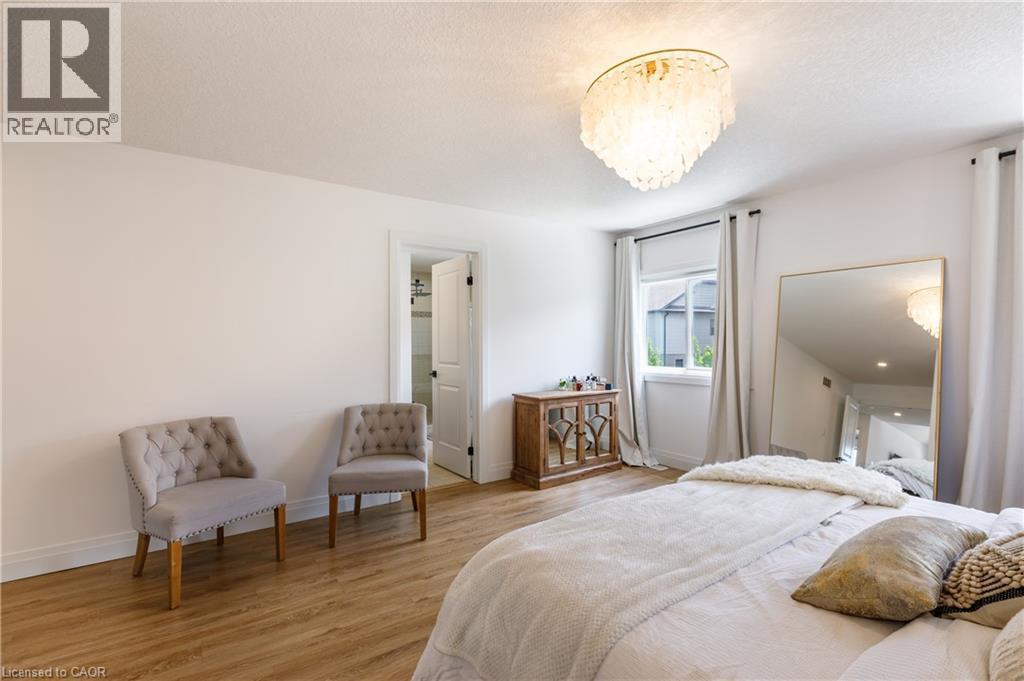 Spacious room with wood-finish flooring, a contemporary chandelier, a window with roller blinds, and an open doorway revealing a partial bathroom - 916 Steepleridge Court, Kitchener, ON - Indoor Photo Showing Bedroom
