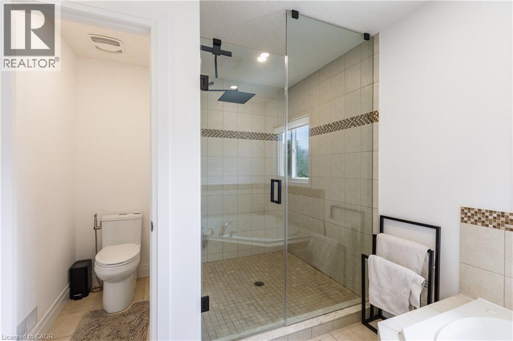 Glass-enclosed shower with tile surround and mosaic accent band, featuring a dark-finish rain shower head - 916 Steepleridge Court, Kitchener, ON - Indoor Photo Showing Bathroom