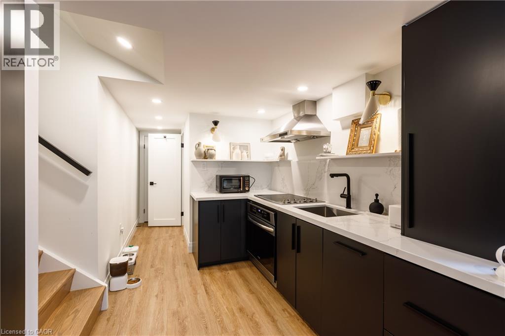Contemporary kitchen featuring dark flat-panel cabinetry, light stone-finish countertops, a stainless steel range hood, and a matte black faucet - 916 Steepleridge Court, Kitchener, ON - Indoor Photo Showing Kitchen