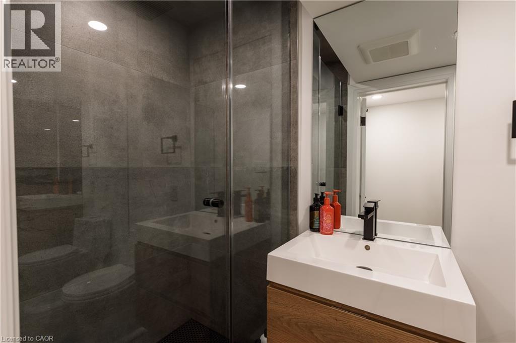 Contemporary bathroom featuring a floating wood-finish vanity with an integrated white sink, matte black faucet, and a large mirrored wall - 916 Steepleridge Court, Kitchener, ON - Indoor Photo Showing Bathroom