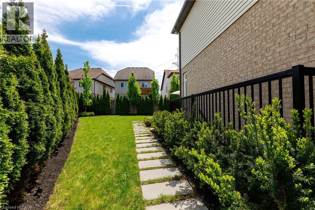 Lush green lawn with a stone paver pathway bordered by mature evergreen shrubs and a parallel row of tall privacy evergreens - 916 Steepleridge Court, Kitchener, ON - Outdoor