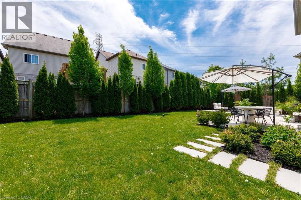 Expansive backyard featuring a manicured lawn, a large patio with a dining area, and concrete stepping stones - 916 Steepleridge Court, Kitchener, ON - Outdoor