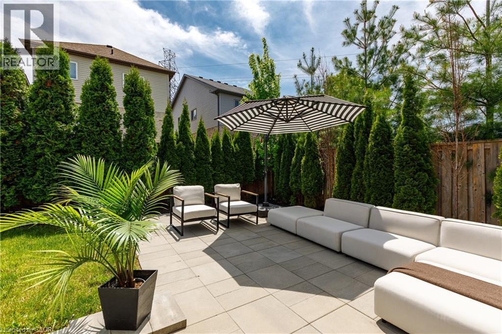 Patio area featuring pavers, an attached privacy fence, mature evergreen trees, and a manicured lawn - 916 Steepleridge Court, Kitchener, ON - Outdoor