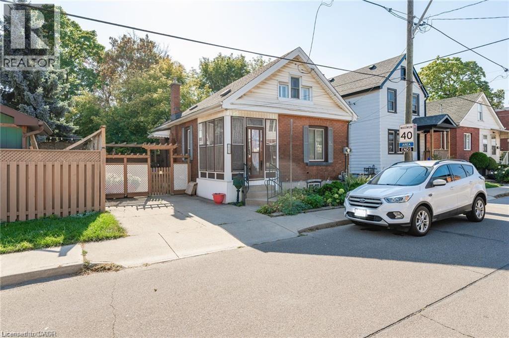 Brick and siding exterior featuring a covered porch, front yard landscaping, a driveway, and a wood privacy fence - 252 Beechwood Avenue, Hamilton, ON - Outdoor With Facade
