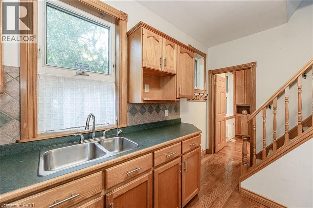 Kitchen area featuring wood cabinetry with silver hardware, a dual-basin stainless steel sink, and a dark countertop - 252 Beechwood Avenue, Hamilton, ON - Indoor Photo Showing Kitchen With Double Sink