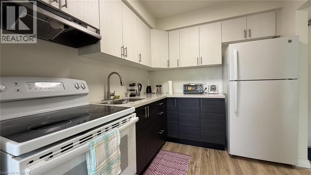 Efficient kitchen featuring white appliances, two-tone cabinetry with light upper and dark lower units, a double basin stainless steel sink with a high-arc faucet, and wood-finish flooring - 206 Indian Road, Kitchener, ON - Indoor Photo Showing Kitchen With Double Sink