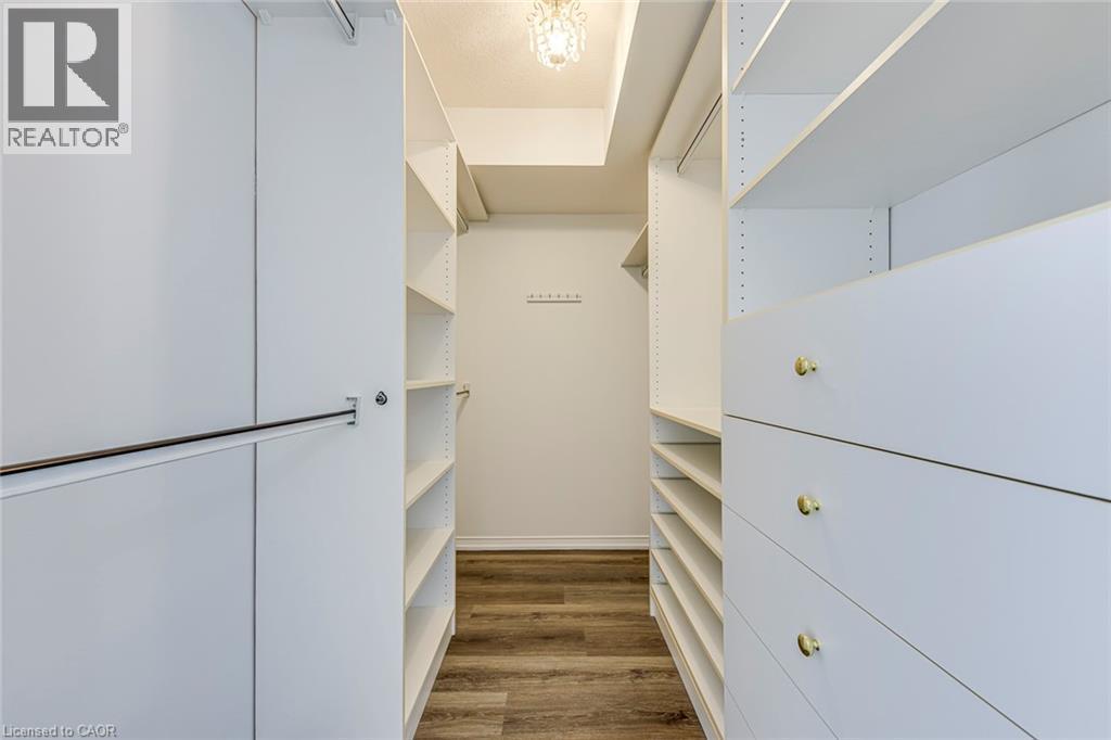Walk-in closet featuring custom white cabinetry, multiple shelves, integrated drawers with gold-toned hardware, and wood-finish flooring - 1270 Maple Crossing Boulevard Unit# 1705, Burlington, ON - Indoor Photo Showing Other Room
