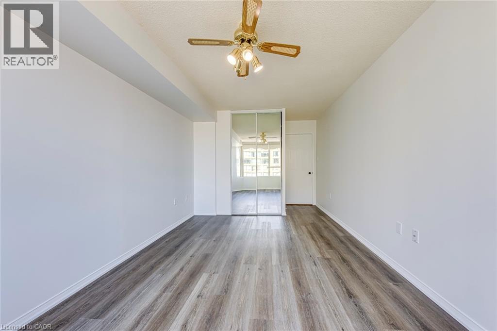 Expansive room featuring wood-finish flooring, white painted walls, a sliding mirrored closet, a recessed ceiling beam, and a ceiling fan with integrated lighting - 1270 Maple Crossing Boulevard Unit# 1705, Burlington, ON - Indoor Photo Showing Other Room