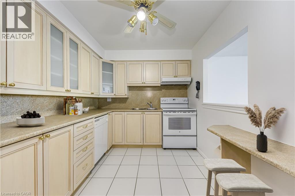 Kitchen featuring extensive cabinetry, tile flooring, a built-in oven range, and a breakfast bar with seating - 1270 Maple Crossing Boulevard Unit# 1705, Burlington, ON - Indoor Photo Showing Kitchen