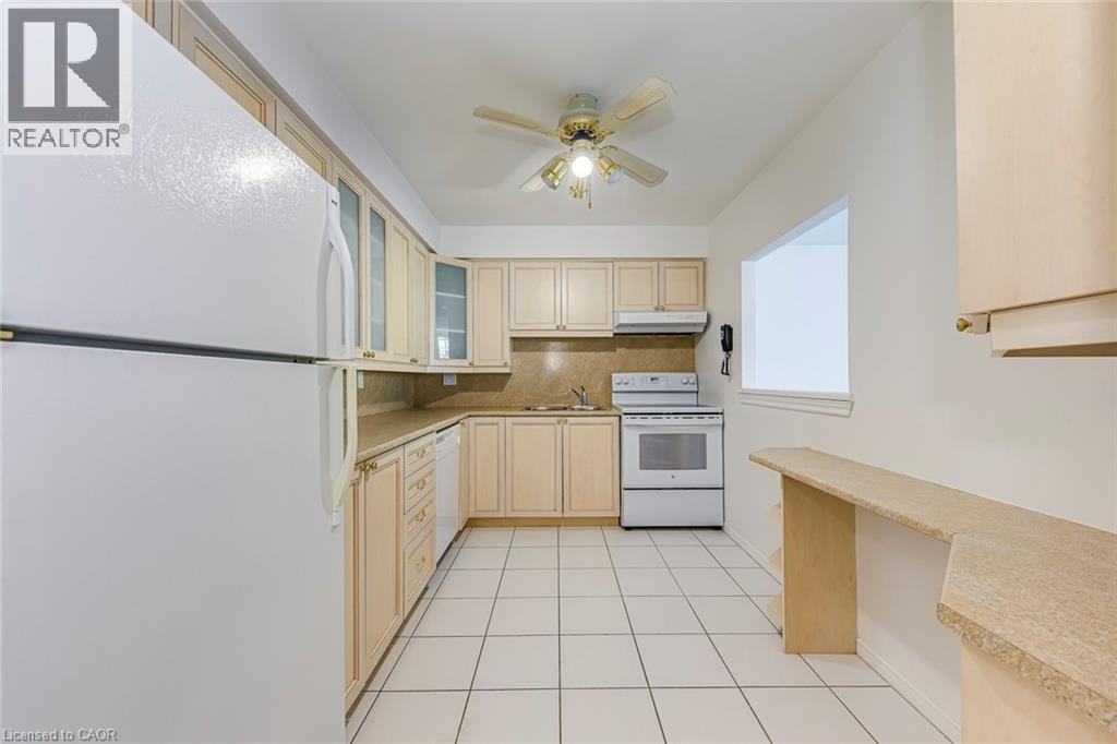 Functional kitchen featuring white appliances, light wood-finish cabinetry with glass accents, and a complementary stone-finish countertop - 1270 Maple Crossing Boulevard Unit# 1705, Burlington, ON - Indoor Photo Showing Kitchen