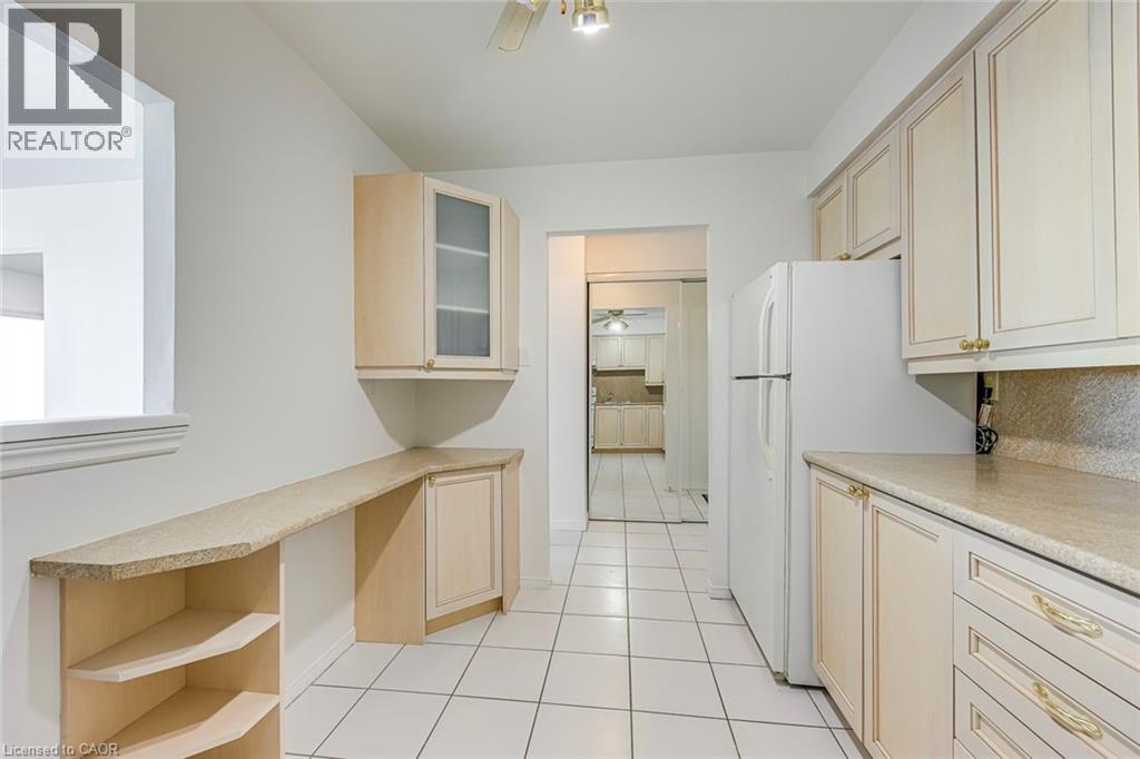Kitchen featuring white square tile flooring, light-toned cabinetry, light-toned countertops, and a full-size white refrigerator - 1270 Maple Crossing Boulevard Unit# 1705, Burlington, ON - Indoor Photo Showing Kitchen