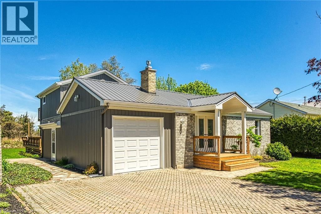 Brick and vertical siding exterior featuring a metal roof, attached garage with white door, and a front porch with natural wood decking and railings - 270 Erie Boulevard, Long Point, ON - Outdoor With Deck Patio Veranda