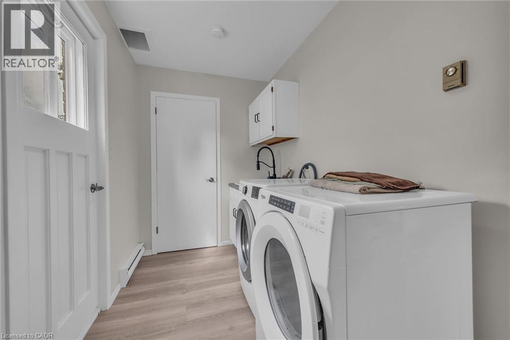 Dedicated laundry area featuring wood-finish flooring, white cabinetry, and a utility sink with a matte black faucet - 270 Erie Boulevard, Long Point, ON - Indoor Photo Showing Laundry Room