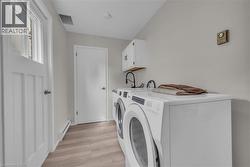 Dedicated laundry area featuring wood-finish flooring, white cabinetry, and a utility sink with a matte black faucet -