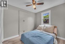 Room featuring wood-finish flooring, light grey walls, white trim, a built-in wardrobe, and a ceiling fan with light fixture -