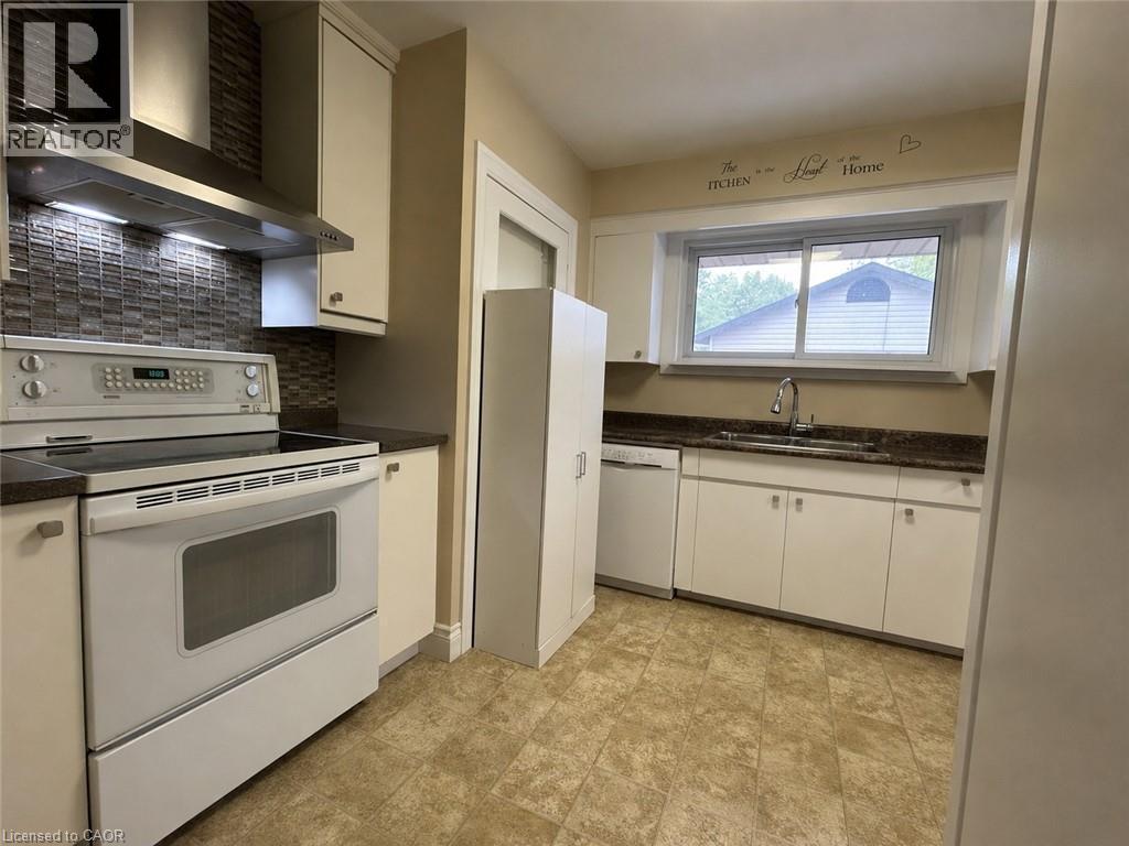 Kitchen featuring a mosaic tile backsplash, stainless steel range hood, ample white cabinetry, dark countertops, and resilient flooring - 917 Orpha Street, Burlington, ON - Indoor Photo Showing Kitchen With Double Sink