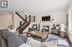 Living space featuring a stone-clad fireplace with a decorative mantle, recessed lighting, crown molding, a dark wood-finish staircase with wrought iron spindles, and wood-finish flooring. -