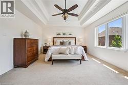 Spacious primary featuring a tray ceiling with a ceiling fan, light-toned carpeting, and a large multi-pane window. -