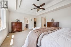 Primary Bedroom featuring a tray ceiling with crown molding, ceiling fan with integrated lighting, broad window, and carpet flooring. -