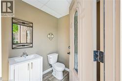 Outdoor powder room featuring a white single-sink vanity, coordinating toilet, and wood-finish flooring. -