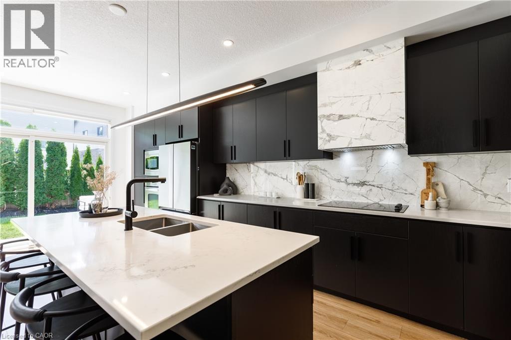 Modern kitchen featuring dark cabinetry, white countertops, and a full-height backsplash with a marble-like pattern - 916 Steepleridge Court, Kitchener, ON - Indoor Photo Showing Kitchen With Double Sink With Upgraded Kitchen