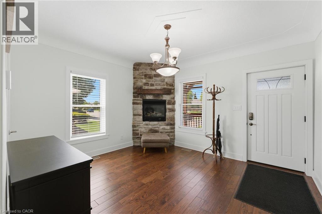 Entryway featuring a corner stone fireplace with a wood mantle, rich wood-finish flooring, and crown molding - 69 Nash Road S, Hamilton, ON - Indoor With Fireplace