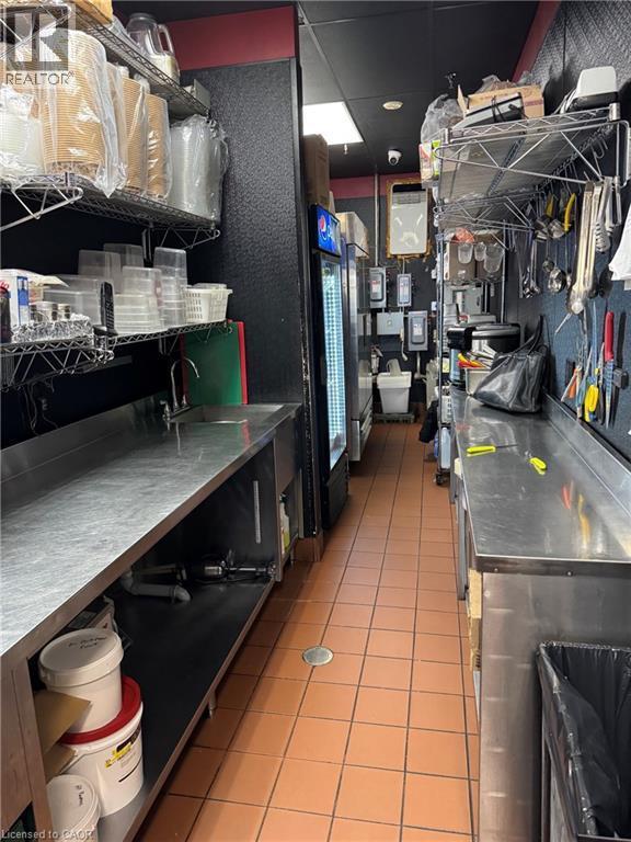 Commercial kitchen space featuring stainless steel countertops, built-in shelving, tiled flooring, and a beverage cooler - 255 King Street N, Waterloo, ON