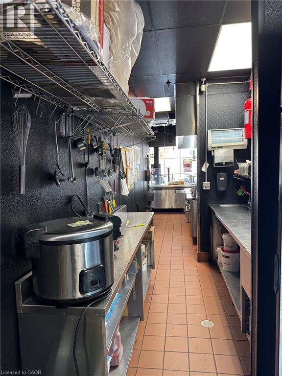 Commercial kitchen featuring stainless steel countertops, tile flooring, and overhead lighting - 255 King Street N, Waterloo, ON