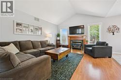 Living area featuring vaulted ceilings, wood-finish flooring, a fireplace with a wood mantle and tile surround, and multiple windows -
