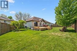 Expansive grassy lawn bordered by a wood fence, featuring a multi-level wood deck with steps, and mature trees -