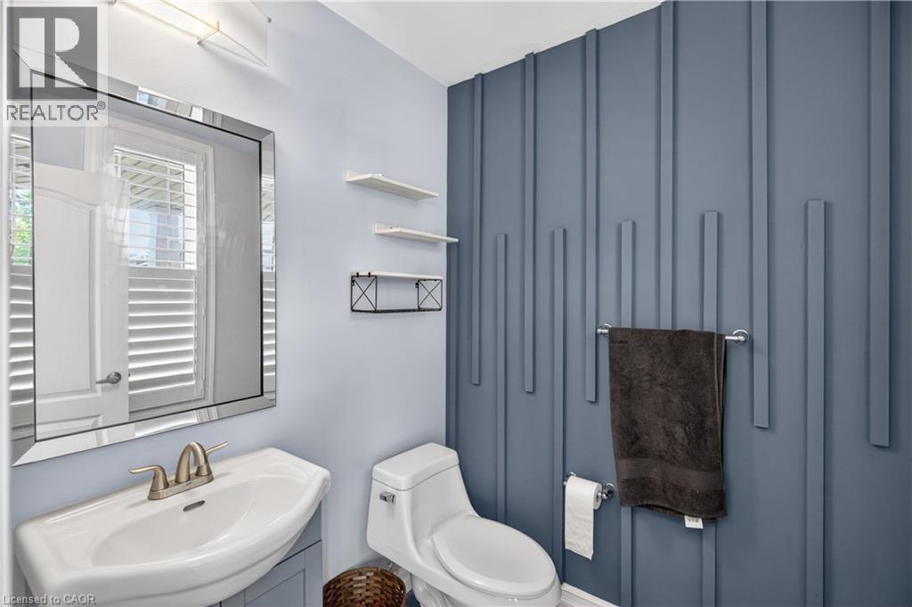 Contemporary powder room featuring a decorative accent wall with vertical paneling, a wall-mounted sink with brushed nickel faucet, a frameless beveled mirror, and recessed lighting - 9 Fleming Crescent, Caledonia, ON - Indoor Photo Showing Bathroom