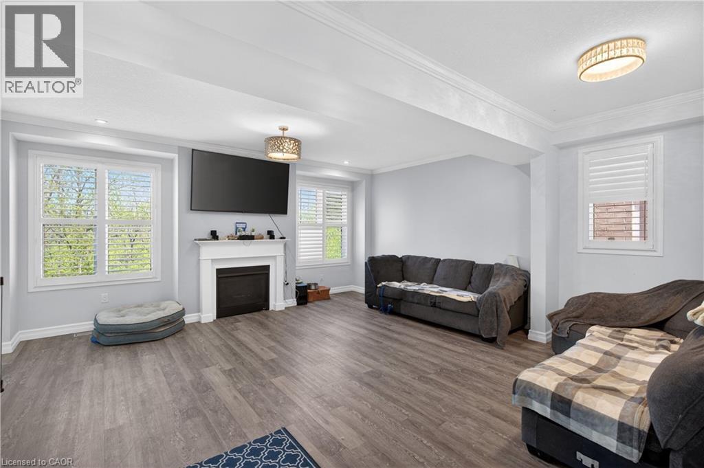 Spacious living area featuring wood-finish flooring, a white mantel fireplace, and two windows with white plantation shutters - 9 Fleming Crescent, Caledonia, ON - Indoor Photo Showing Living Room With Fireplace