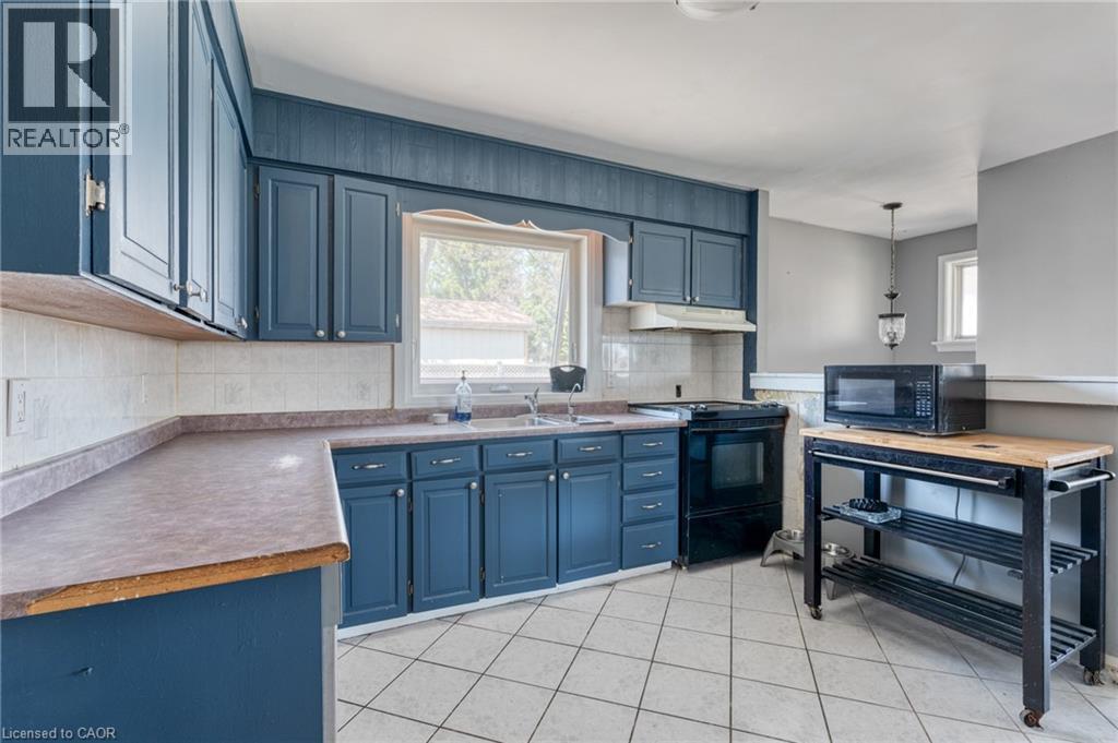 Kitchen featuring blue cabinetry, light tile flooring, a window above the sink, a black range, and a tile backsplash - 151 Winchester Boulevard, Hamilton, ON - Indoor Photo Showing Kitchen