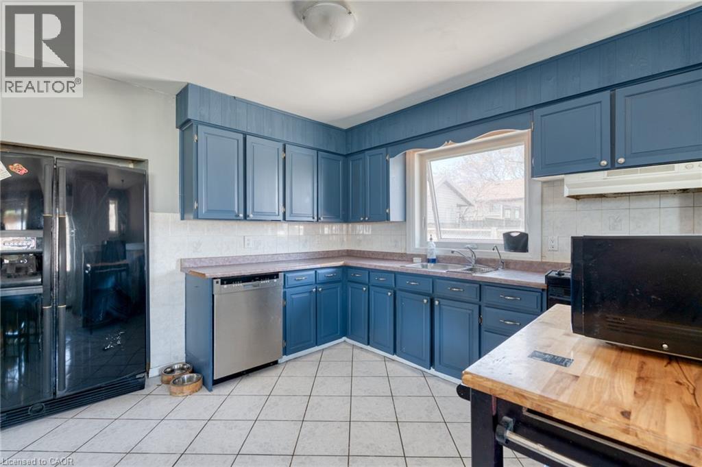 Kitchen featuring blue cabinetry, a stainless steel dishwasher, a black side-by-side refrigerator, white tile flooring, and a window above the sink - 151 Winchester Boulevard, Hamilton, ON - Indoor Photo Showing Kitchen