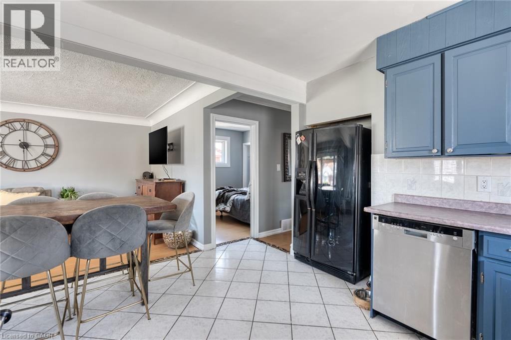 Kitchen area featuring white square tile flooring, blue cabinetry, a light-colored backsplash, and a stainless steel dishwasher - 151 Winchester Boulevard, Hamilton, ON - Indoor Photo Showing Kitchen