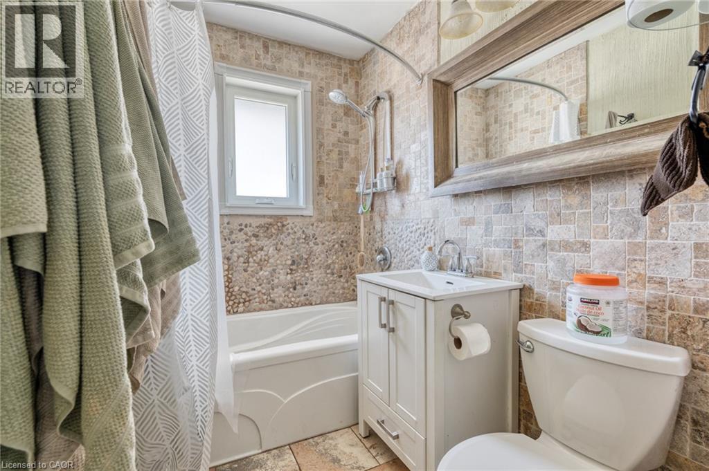 Bathroom featuring full wall tile, a single vanity with storage, an integrated sink, a built-in bathtub with shower, and a window - 151 Winchester Boulevard, Hamilton, ON - Indoor Photo Showing Bathroom