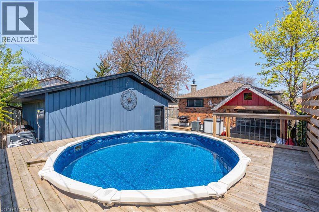 Outdoor entertaining space featuring a round above-ground pool, expansive wood decking, and a red-accented pool house with a covered patio - 151 Winchester Boulevard, Hamilton, ON - Outdoor With Above Ground Pool With Deck Patio Veranda