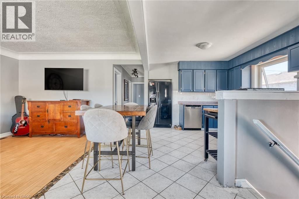 Kitchen and living area featuring a wood-finish flooring, tiled kitchen flooring, blue cabinetry, stainless steel dishwasher, and a window above the sink - 151 Winchester Boulevard, Hamilton, ON - Indoor Photo Showing Other Room