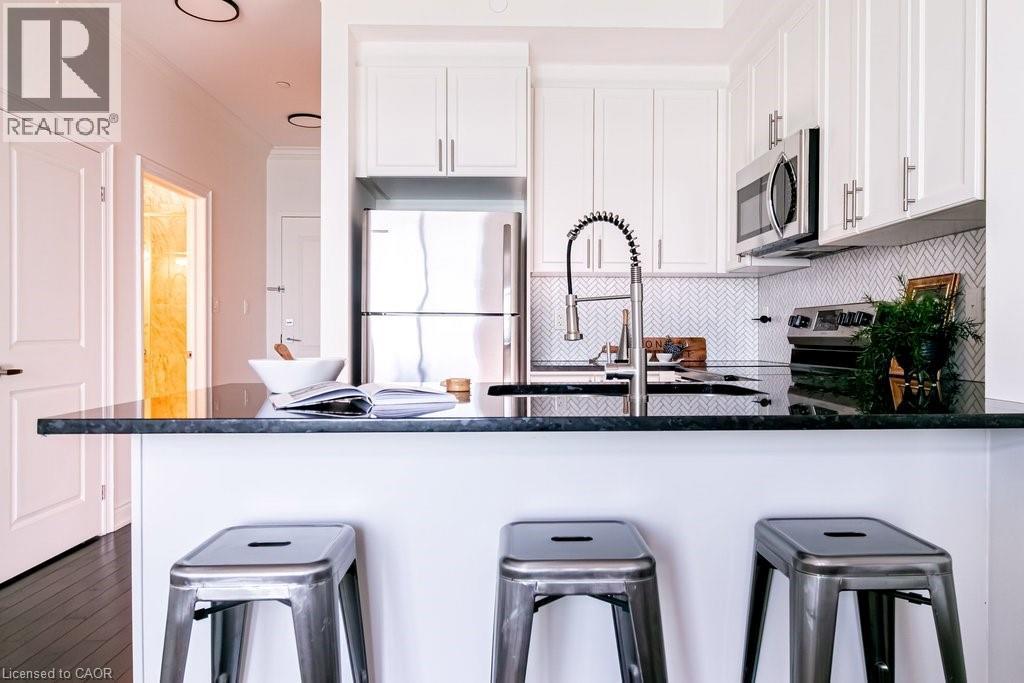 Kitchen featuring stainless steel appliances, dark countertops, white shaker cabinetry, a herringbone tile backsplash, and dark wood-finish flooring - 101 Shoreview Place Unit# 631, Stoney Creek, ON - Indoor Photo Showing Kitchen