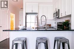 Kitchen featuring stainless steel appliances, dark countertops, white shaker cabinetry, a herringbone tile backsplash, and dark wood-finish flooring -