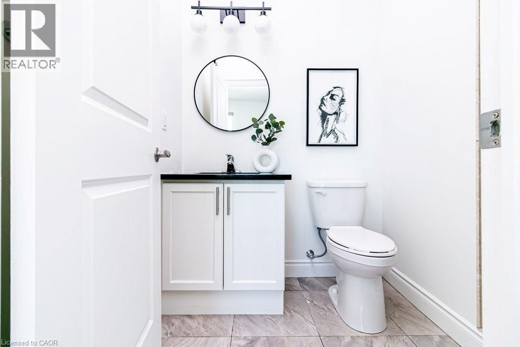 White vanity with black countertop and chrome faucet, under a circular mirror with black frame - 101 Shoreview Place Unit# 631, Stoney Creek, ON - Indoor Photo Showing Bathroom